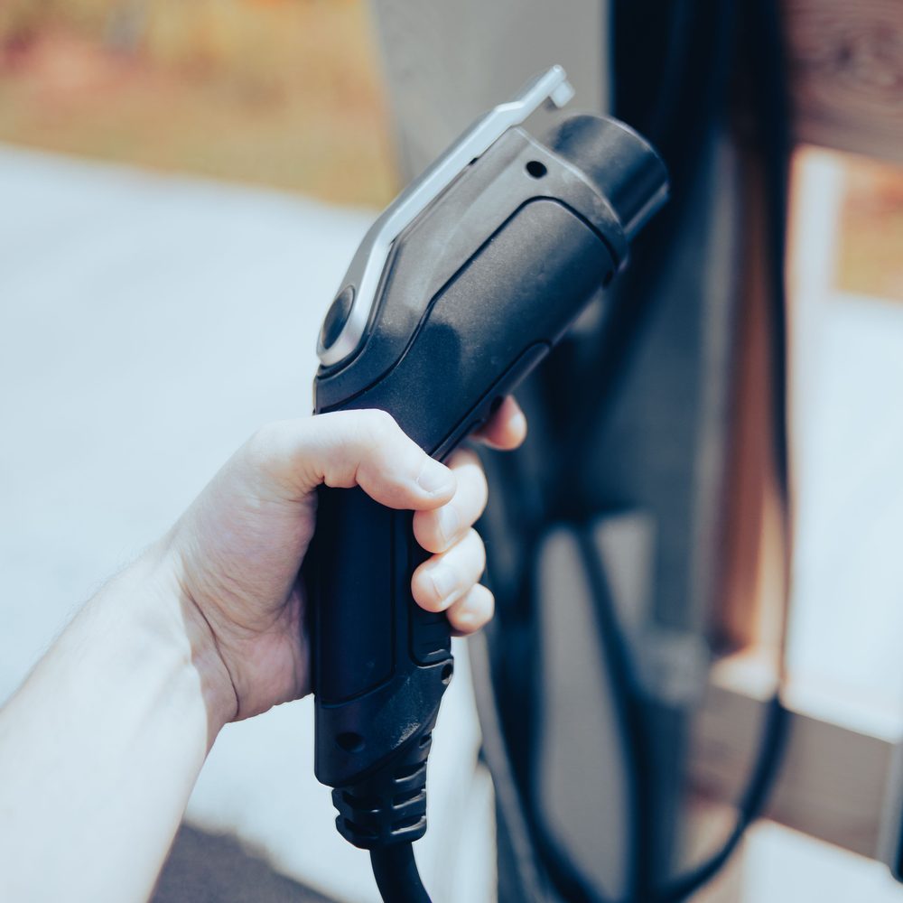 A hand holding a J1772 charging connector at a public charger
