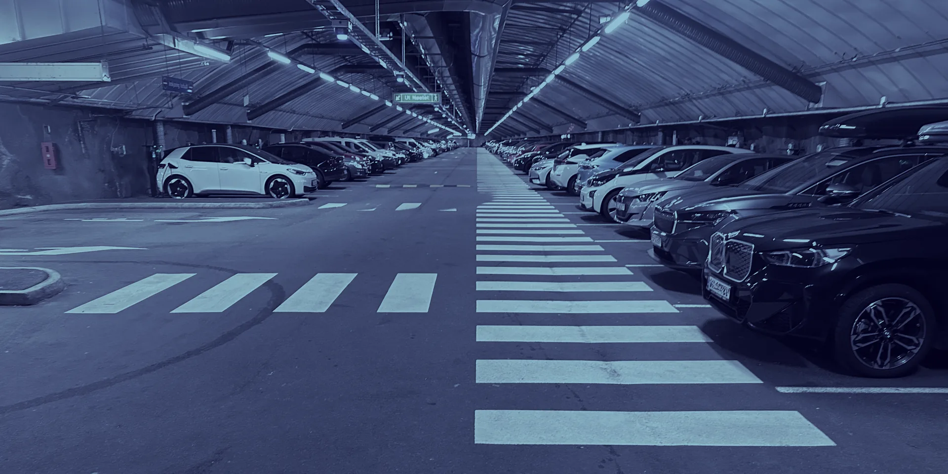 A property manager checking a tablet beside an electric car on charge in a parking structure